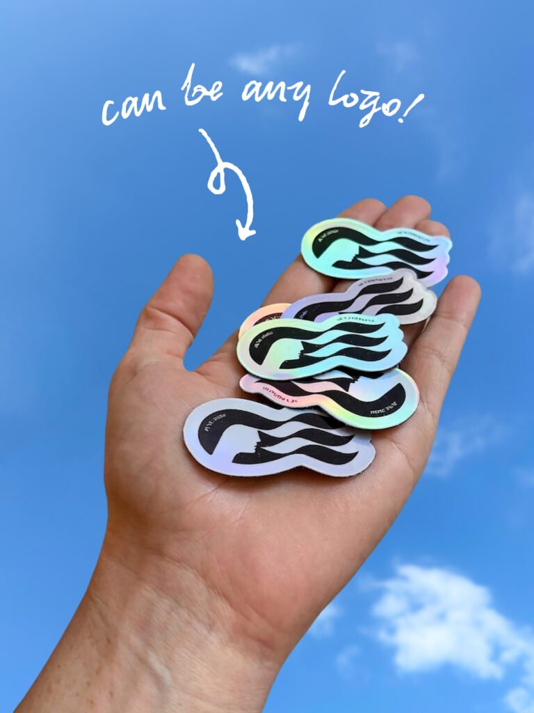 Person holding a stack of holographic stickers with a black wavy design against a blue sky backdrop; handwritten text above reads 'can be any logo!'