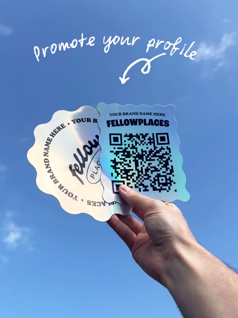 Hand holds two scalloped promotional badges with a QR code and placeholder brand name against a blue sky background